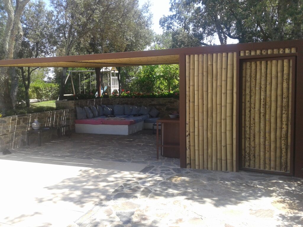 Pérgola de hierro con techo de bambú guadua natural y baño exterior revestido con cañas de bambú